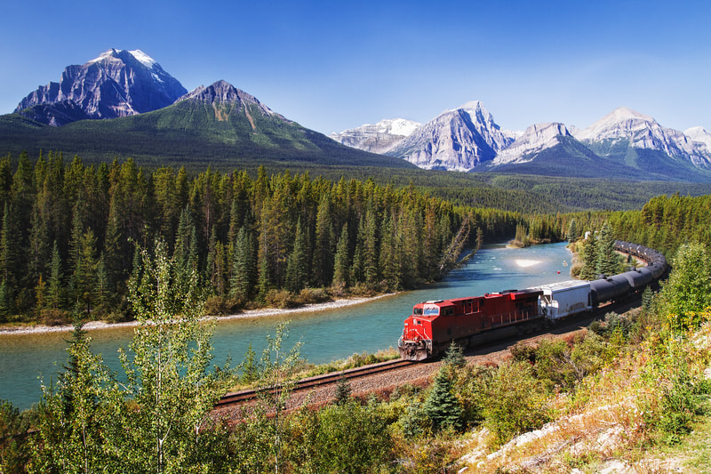 Train crossing across a forest with the mountains on the background. 